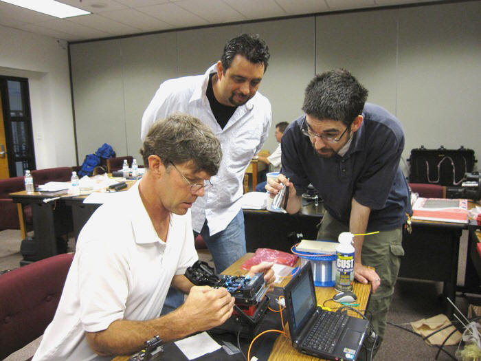 Phil Graham works on a fusion splice while Luis Torres (left) from District 10 and Michael Mullen (holding a light) from District 3 watch and talk through the exercise with Phil.