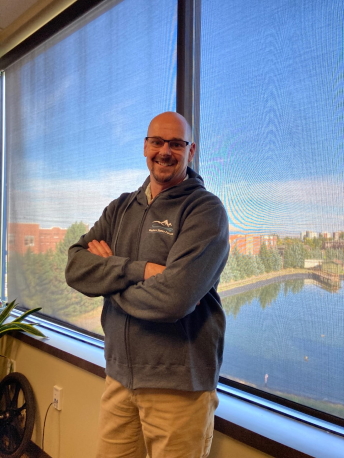 A man stands in an office wearing a Western States Forum zippered hoodie sweatshirt