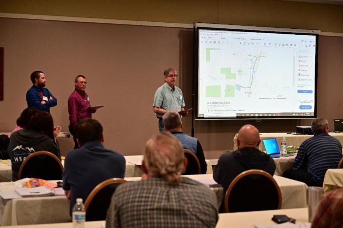 Three men stand in front of a projector screen.