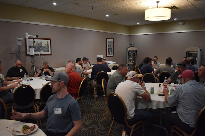 Groups of people eating at round tables. In the background are two ITS cabinets and two cameras mounted on stands.