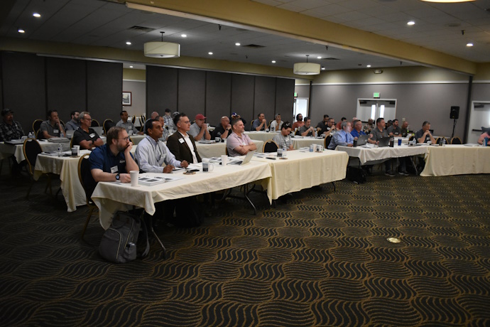 A group of people seated at rectangular tables in rows.