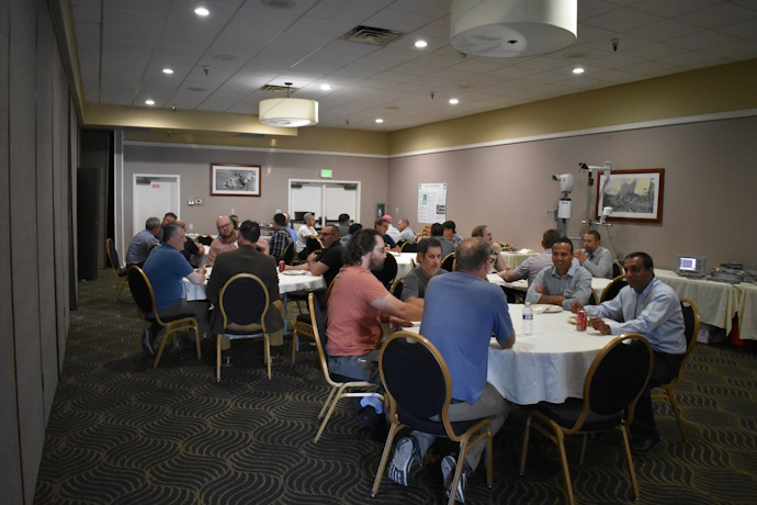 Six groups of people eating and talking together at round tables.