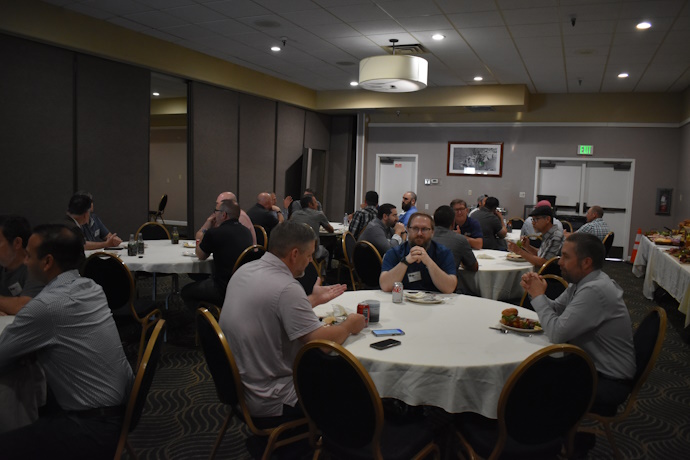 Five groups of people eating and talking together at round tables, a buffet of food on the side.