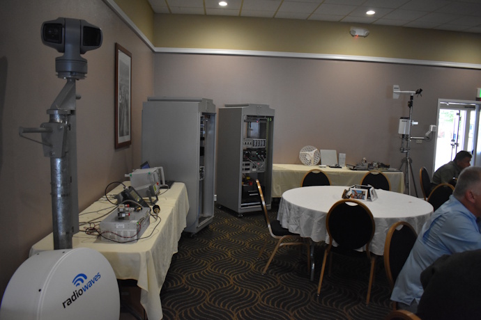 Two ITS cabinets, 'radiowaves' dish, weather station, radio antennas, mounted CCTV camera, electronics equipment on a table. Display.